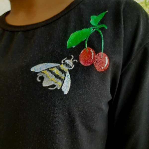 Black shirt featuring embroidered bee and cherry artwork detail