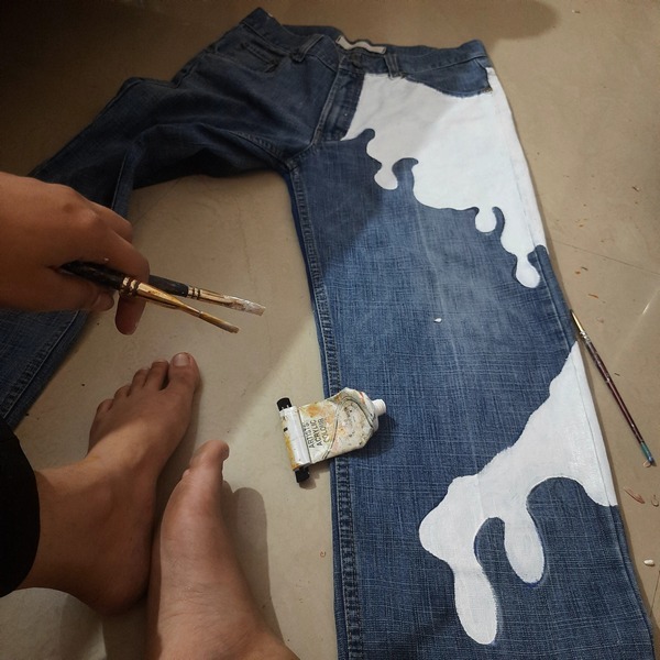 Artist hand-painting custom white artwork on dark denim fabric