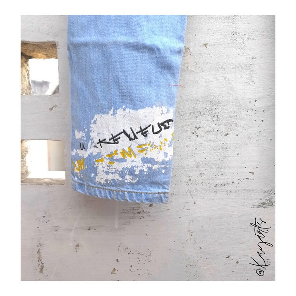 Close-up of painted and embroidered artwork on denim jean cuff